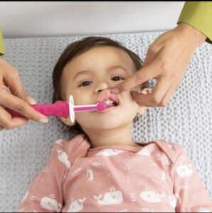 bebe tumbado su madre levanta el labio superior para poder realizar el cepillado dental